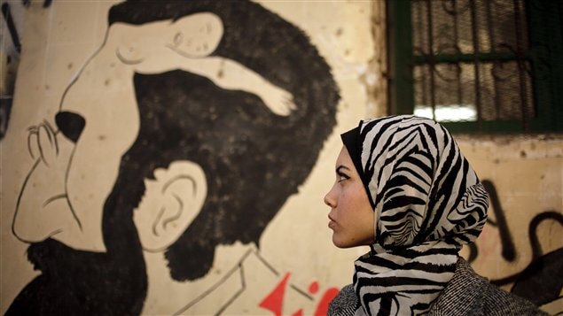 مغنية الراب المصرية ميام محمود تقف أمام عدسة المصورة قرب لوحة جدارية تظهر جسد امرأة عارية على رأس رجل، في وسط القاهرة في 10 كانون الأول (ديسمبر) الفائت 