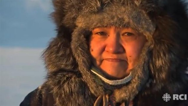 A close up picture of an Inuk woman wearing a parka with a fur-lined hood. 