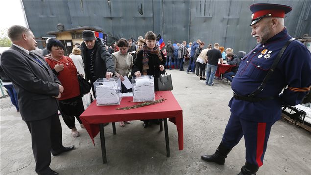 Des citoyens votent sous le regard attentif d'un garde à Donetsk. 