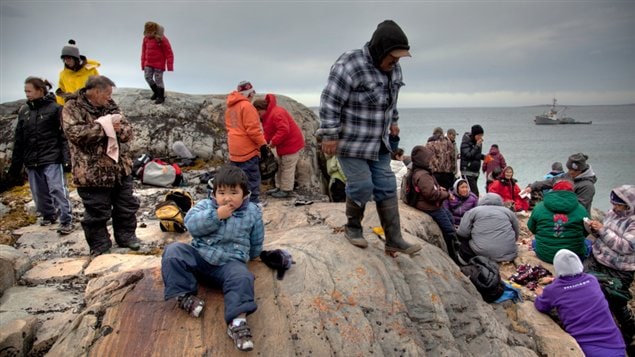 A still photograph from the web documentary Iqqaumavara depicting Inuit residents of Inukjuak, Quebec on rock near the water. 