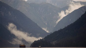 Barges make their way across water amid high, cloud-covered BC mountains.