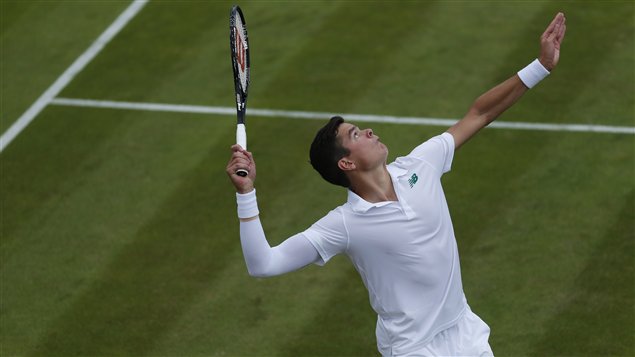 Milos Raonic in Wimbledon whites reaches up to crush a serve.