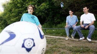A 10-year-old kicks a soccer ball in the foreground to the delight on his father and brother. Coaches are working hard to deal with the ill-effects of concussions.