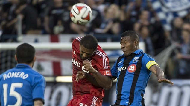 Toronto FC's Luke Moore in a red jersey heads the ball away from Montreal Impact's Patrice Bernier in a Montreal blue with stripes jersey during first half Voyageurs Cup action earlier this month in Montreal. 