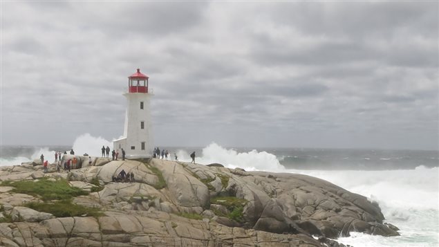 Show of lighthouse on coastal rocks surrounded by giant waves.