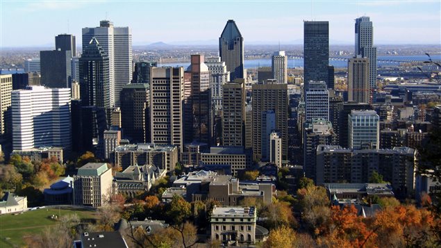 A shot of Montreal from the mountain lookout with the city's tallest buildings in the foreground and the St. Lawrence River and the fields of the province in the distance.