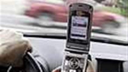 riving while texting is proving extremely dangerous. Photo shows a closeup of a smartphone in a driver's right hand with his left hand on the wheel. A red pickup truck is shown speeding by his front window.