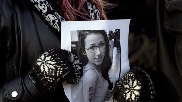 A woman holds a photo as several hundred people attend a community vigil to remember Rehtaeh Parsons at Victoria Park in Halifax in April of last year. The girl's family said she ended committed suicide following months of bullying after she was allegedly sexually assaulted by four boys and a photo of the incident was distributed. The photo shows a teen-age girl with a gentle face wearing eye glasses. She is in a summer dress with straps over her shoulders. We do not see the woman holding the picture other than her mittens and scarf over a black topcoat.