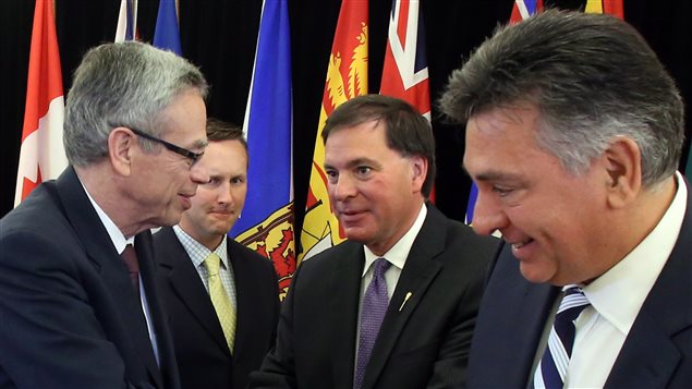Finance Minister Joe Oliver, left, shakes hands with Saskatchewan Justice Minister Gordon Wyant, centre right, as New Brunswick Justice Minister Troy Lifford, centre left, and Ontario Finance Minister Charles Sousa look on at a news conference after signing an agreement to move towards a co-operative capital markets regulatory system in Ottawa on Wednesday. All the men are dressed alike in dark suits and dress shirts. There are small glimpses of provincial flags behind them.