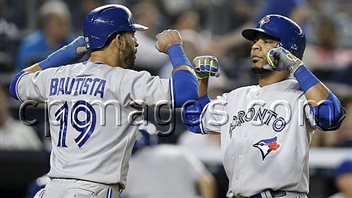 Toronto Blue Jays Jose Bautista celebrates with teammate Edwin Encarnacion after scoring on Encarnacion's eighth-inning two-run homer against the Yankees in New York in June. Bautista is at the left of the pitcher, Encarnacion on the right. They are about fist bump in celebration. Encarnacion is out of the lineup indefinitely with leg problems.