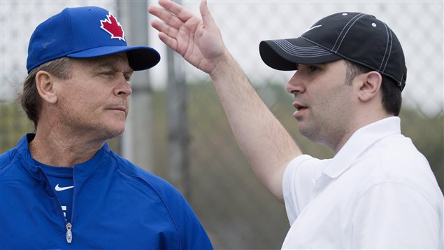 Blue Jays GM Alex Anthopoulous, right, and manager John Gibbons have a lot to chew on as the team heads into the second half of the season. In the photo, Anthopoulos has on a dark blue baseball cap. He is in a dress shirt and gesturing with his right hand. Gibbons is wearing a lighter blue Blues Jays cap and a blue warmup jacket with Blue Jays written on the front. The two are standing in front of a batting cage.