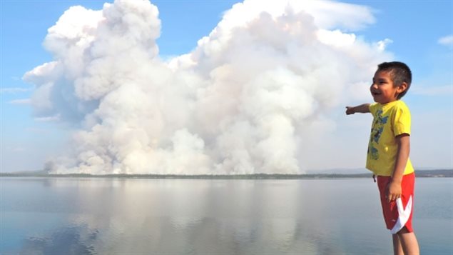  Un jeune garçon pointant un feu de forêt faisant rage de l'autre côté du lac près de Gameti dans les TNO 