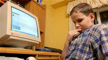 Timothy Peters tries to figure out a brain-teaser on a Canadian National Institute for the Blind website, the Children's Discovery Portal. The site allows blind children to chat with one another, swap jokes, and participate in a number of online activities. The boy, about eight or nine it appears, is sitting in desk chair and has his right hand to his chin as he attempts to work out something in his mind. He has short brown hair and is looking slightly down. The computer looms to his right on a desk. Behind him is a tan wall.