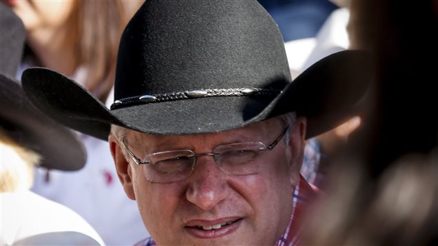 Prime Minister Stephen Harper attends the Calgary Stampede parade earlier this month. New research suggests Mr. Harper's Tories may not be on the same page with much of the public. Harper is shown in a closeup shot of his head (what the Cockneys call a 'full boat'). He is wearing a black cowboy hat with a narrow band and rimless glasses and is looking to his left listening to a comment.