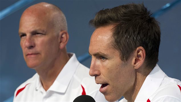 Can Basketball Canada general manager Steve Nash, right, and head coach Jay Triano lead the Canadian national team to greater glory by qualifying for the 2016 Rio Olympics? Nash has short black hair and is speaking into a microphone with great intensity. Triano sits quietly to his left, listening. He is a bald man, older than Nash, who is 40. Each is wearing a Team Canada white polo shirt.