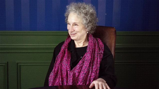 Writer Margaret Atwood poses for a photo as she promotes her new book "MaddAddam" in Toronto last year. This week Ms. Atwood sharply criticised of the Canada's Conservative government for an audit of PEN Canada, of which she is a member. She is seen from the right sitting behind what appears to be an oak table wearing a pink scarf over either a black dress or black top. She has dark grey curly hair and a kind face. She appears to be listening to a question from her audience. 