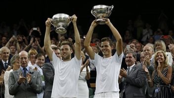 Vasek Pospisil, right, and Jack Sock of the U.S. hold up their trophies after defeating the Bryan twins in the men's doubles at Wimbledon this summer. Pospisil and Sock will play together at the Rogers Cup in Toronto. Both are holding their large blowl-shaped silver trophies high above their heads with both hands. Both are flashing very winning smiles. Both are dressed in white. Sock has something resembling a long crew cut with hints of dye job at the top. Pospisil hair is more traditionally groomed with the part on the left. Both are trending blond. At he the left the photo, the Duke of Kent, wearing a grey suit, applauds. The duke is balding and has a very serious expression on his face as his mouth, slightly agape, dips down from a stiff upper lip to a prominent chin.
