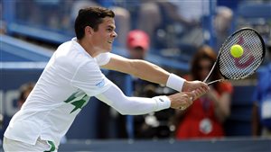 Milos Raonic, hitting his two-handed backhand, used his big serve to dominate compatriot Vasek Pospisil during the men's singles final in Washington. Raonic is reaching to his left. His right arm is covered by an elastic sleeve. His mouth is slightly open.