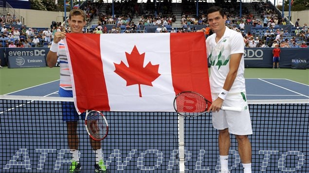 It was Canada Day in Washington as Vasek Pospisil, left, and Milos Raonic pose before the men's singles final at the Citi Open tennis tournament on Sunday. Raonic is in white, standing on the near side of the net. Pospisil, in blue shorts and a multi-caloured shirt, stands at the far side of the net. They are holding the Canadian flag. They stand on a dark blue hard court, similar to the ones in Toronto and Montreal.