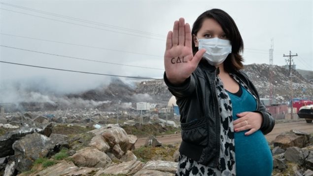 Julie Alivaktuk devant le dépotoir qui brûle à Iqaluit au Nunavut. Dans sa main, il est écrit «Taima », « ça suffit ». 