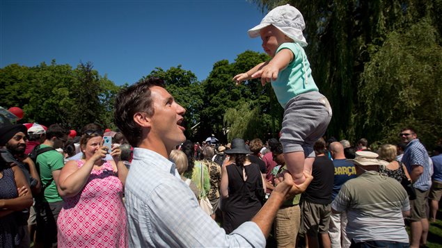 Liberal Leader Justin Trudeau balances his 5-month-old son Hadrien on his hand while attending Liberal barbeque in Vancouver earlier this month. Mr. Trudeau is wearing a light blue sports shirt and holding Hadrien by the feet with his right hand. He is smiling at the baby who is looking at his dad with just a tad of bewilderment. Hadrien's arms are extended outward for balance. He is wearing a white sun hat and white shirt.