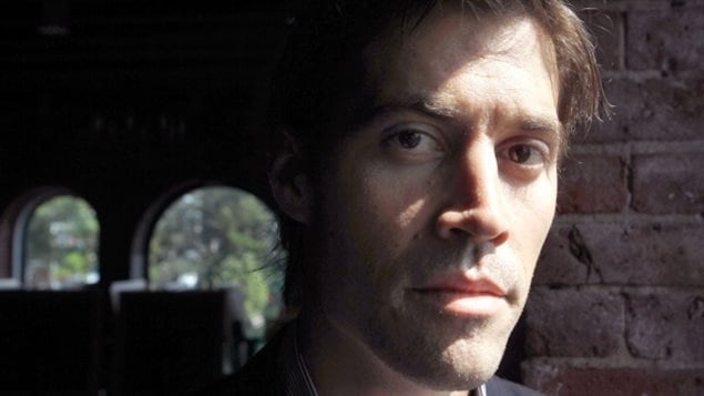 James Foley was kidnapped in November 2012 and held in captivity until he was executed by ISIS militants this week. The group released a video purporting to show Foley’s killing. Mr. Foley has a long, handsome face with a prominent chin and light brown hair. The photo shows him from the chin up looking directly at the camera through large, gentle brown eyes below somewhat busy eyebrows. The photo is dark in texture as Foley stands in front of a brick wall with rounded windows in the background behind his right shoulder.