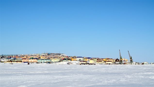 A picture of the skyline of the Arctic Russian town of Anadyr. The distant view of the town is sandwhiched between blue sky and white snowy ground. 