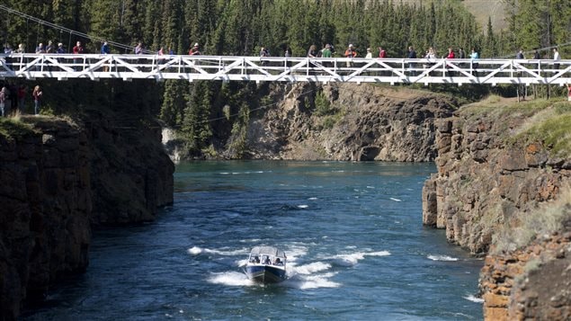 Stephen Harper and wife, Laureen, take a boat up the Yukon river under the Miles Canyon suspension bridge in Whitehorse on Friday. We see a blue and white speedboat approaching us, her white wake contrasting with the crystal blue water of the river. The river sits between 30 ft. high gray and mossy rocks. Sitting overhead is a thin white bridge filled with photographers and journalists. We don't actually see that the Harpers are in the boat, but it sure is a pretty picture.