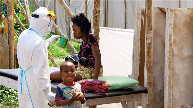 Dans un hôpital gouvernemental du Sierra Leone, un infirmier vêtu d'une combinaison protectrice offre de l'eau à une patiente atteinte de la fièvre d'Ebola.