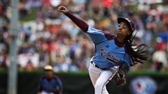 America Mo'ne Davis delivers a pitch at the Little League World Series. Wearing a light blue jersey and white pants, she is letting fly with a fastball, showing perfect form. He braided hair flies out behind her. 