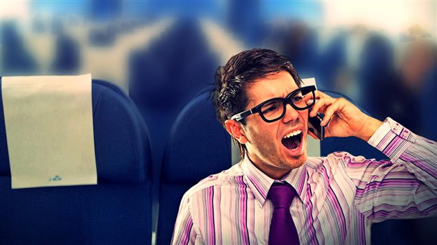 Information overload can lead to some untoward results. We see a man sitting in a blue airline seat. He is wearing very large horn-rim glasses and has a smartphone up to his left ear. His mouth is agape and he appears very frazzled in his purple Windsor-knotted tie and stripped purple and white dress shirt. His black hair is gelled and somewhat messy.