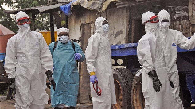 Au Liberia, des travailleurs du réseau de la santé à l'extérieur de la maison d'un homme qui serait mort du virus Ebola. Au Liberia, des travailleurs du réseau de la santé à l'extérieur de la maison d'un homme qui serait mort du virus Ebola.