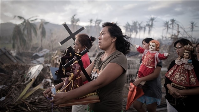 Photo gagnante du World Press Photo dans la catégorie Spots d'information/photo isolée.Dix jours après le passage du typhon Haiyan, des survivants portent des symboles religieux à Tolosa, sur l'île de Leyte, au centre des Philippines. Haiyan, l'un des plus puissants typhons jamais enregistrés, a dévasté 47 provinces, causant un énorme ravage, laissant plus d'un million d'habitations endommagées dont la moitié entièrement détruites, et faisant plus de 4 millions de déplacés. De vastes zones sont restées sans électricité ni eau pendant des semaines, et la destruction des infrastructures a rendu difficiles la distribution de vivres et les soins médicaux. De nombreux habitants sont partis vers des zones moins touchées, comme Manille, la capitale, et certaines villes ont vu le nombre de leurs habitants presque doubler.