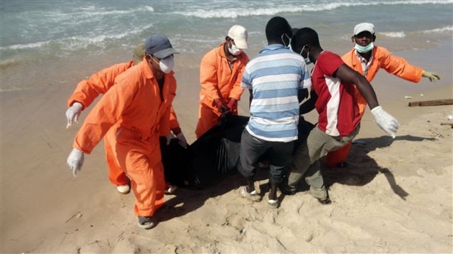 Des secouristes libyens tirent le corps d'un migrant échoué sur la grève.