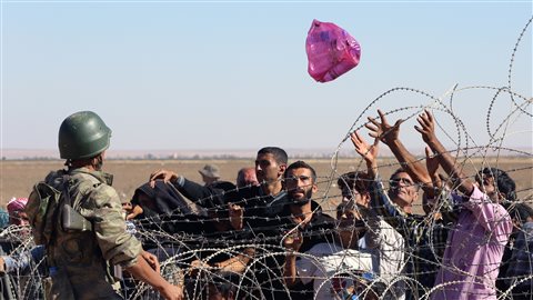 Un soldat turc lance un sac rempli de bouteilles d'eau à un groupe de réfugiés kurdes en provenance de Syrie.