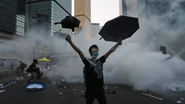 Un manifestant se protège des gaz lacrymogènes à l'aide de deux parapluies à Hong Kong.