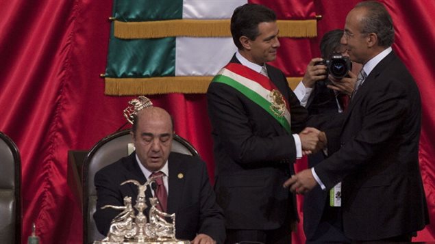El presidente Enrique Peña Nieto aprieta la mano del presidente saliente Felipe Calderón, después de haber recibido la banda presidencial de Jesús Murillo Karam (izq.)