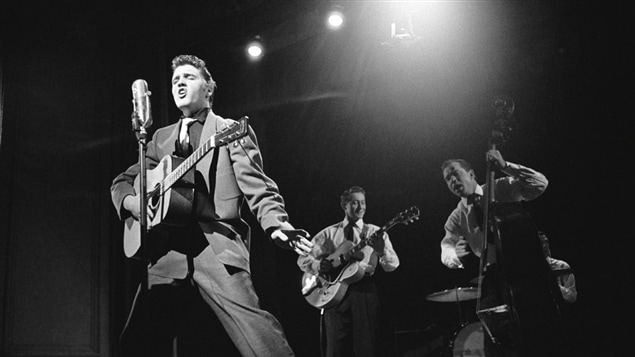 Elvis Presley en concert le 17 mars 1956 avec ses musiciens Scotty Moore (guitare), Bill Black (basse) et DJ Fontana (batterie).