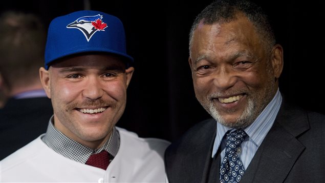 Newly-signed Blue Jays catcher Russell Martin (left) and his father, Russell Martin Sr., a jazz saxophonist, meet the media in November. The younger Martin, one of whose middle names is Coltrane, is being counted on to keep the pitching staff humming into October. Russell Jr. is wearing a white Blue Jays uniform and blue Jays cap with a shirt and tie under the uniform top. His father is dressed to the nines in a three-piece grey suit and fancy shirt and tie. Both have enormous smiles on their faces. Russell, whose mother in French Canadian, has a lighter complexion than his darker-skinned Afro-Canadian father.