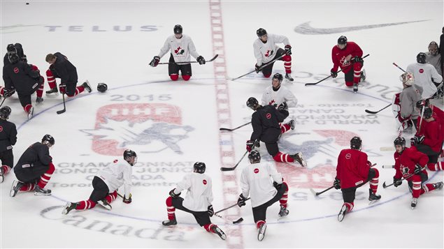Players from Team Canada stretch following a practise session in Montreal on Thursday prior to their first round game Friday against Slovakia at the IIHF World Junior Championship. We see them in white and red sweaters kneeling around the centre-ice face-off circle. 