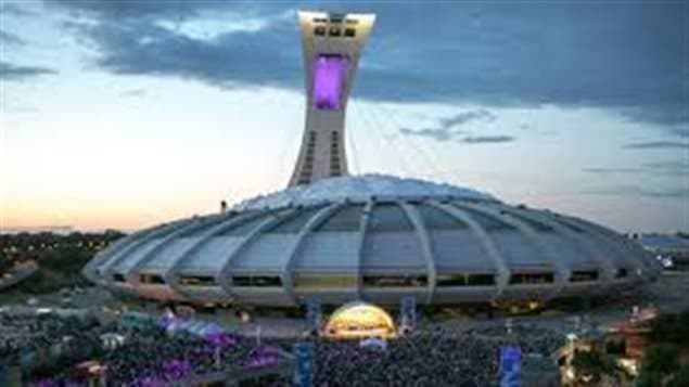  There are many in Montreal who believe fervently that it's only a matter of time before the Olympic Stadium will fill again with baseball fans. We see a long shot of Olympic Stadium with its covered roof topped by its massive tower at dusk under steel sky and purple clouds. A massive crowd in moving toward the facility.