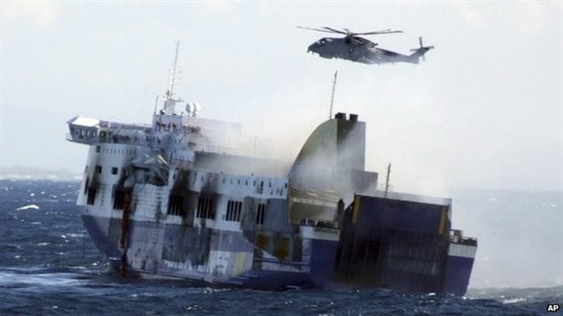 Rescuers faced daunting weather in ferry evacuation. We see the ferry listing to the right and a helicopter hovering above. The seas are high.