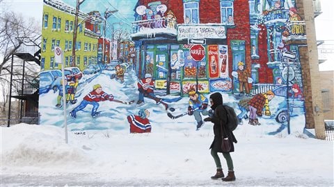 Une piétonne marche devant une murale d'une scène d'hiver à Montréal. 