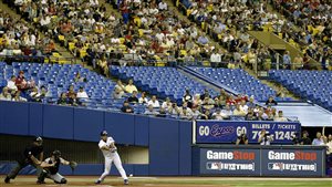 As the team faded in the standings, fewer and fewer fans showed up. The turnouts forced the Expos to move to Washington following the 2004 season. We see a right-handed hitter swinging. Behind his are the catcher and umprire. In the background a blue, mostly empty box seats. The general admission seats are more widely filled.