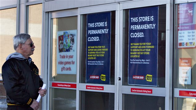 A patron arrives at a Future Shop location in St. Catharines, Ontario on Saturday to discover that all stores in Canada have been closed. We see a grey-haired man in glasses wearing a warmup jacket pondering the sign at the front door of a Future Shop. The sign reads, "This store is permanently closed" in white lettering on a blue base. 