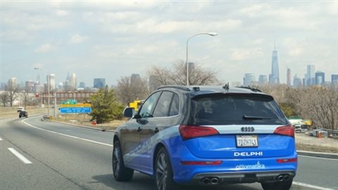 Voiture de conduite automatisée sur l'autoroute avec le profil de la ville de New York au loin.