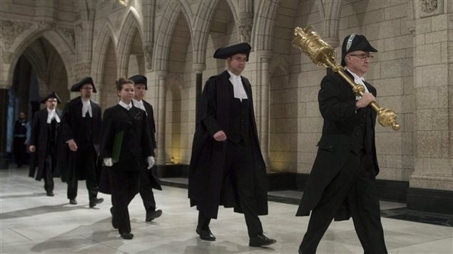 Andrew Scheer, the Speaker of the House of Commons, follows Deputy Sereant at Arms Pat McDonell as he carries a ceremonial mace through the Hall of Honour on Parliament Hill earlier this year. Scheer says daily prayer will remain part of Commons tradition for now. We see black-robed figures walking single-file between the grey walls of parliament. The wooden and ceremonial mace appears to be about feet long. It is being carried by the sergeant at arms on and over his right shoulder. It is of golden colour and has a large round top that becomes a thin handle before expanding at the bottom again. The line is comprised of five men and one woman. She is the only person not wearing a dark hat.