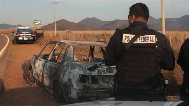 Des agents de la police fédérale mexicaine près d'une voiture incendiée à la suite de l'embuscade d'un convoi de polices à l'extérieur de la ville de Soyatlan près de Puerto Vallarta, le 6 avril 2015.