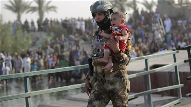 جندي عراقي يحمل طفلاً مهجراً من الرمادي على أحد الجسور القريبة من بغداد في 19 أيار (مايو) الجاري 