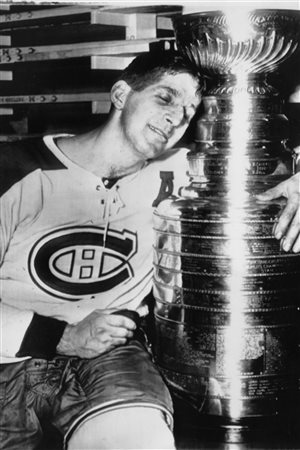 Montreal Canadiens centre Elmer Lach hugs the Stanley Cup in the dressing room of the Montreal Forum in 1953, after scoring the only goal in the fifth game of the Stanley Cup playoffs with the Boston Bruins. We see Lach, appearing completely spent in a black-and-white photo, sitting to the left of the picture with his left hand wrapped around the cup. He is wearing a white sweater with the famed Canadian CH logo as well as an 